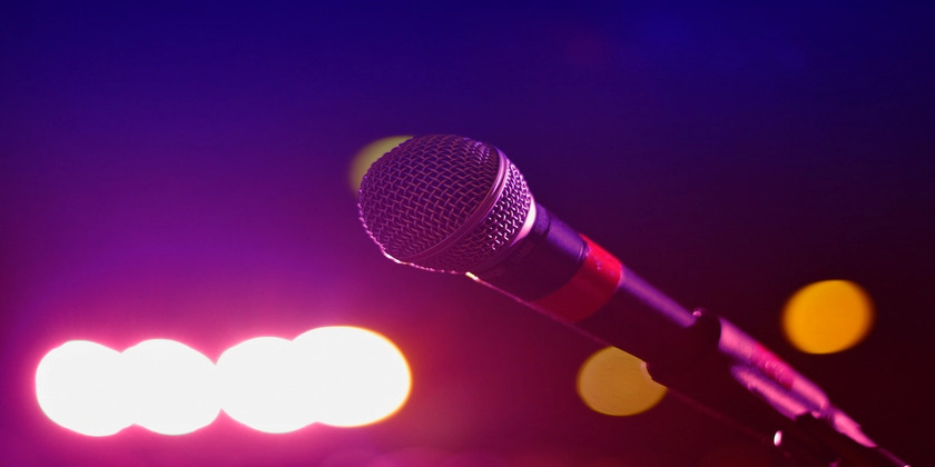 A microphone in front of pink and orange stage lights.