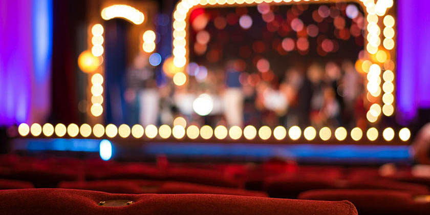 Red seats in a Broadway theatre backlit by stage lights.