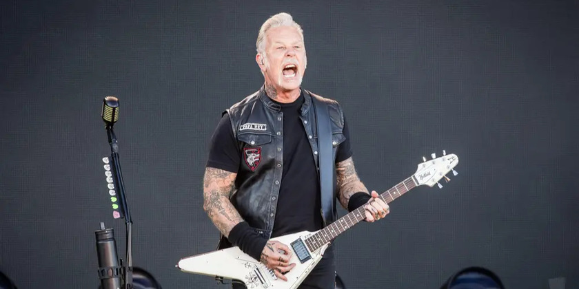 Lead singer of Metallica sings in a leather vest holding a guitar.