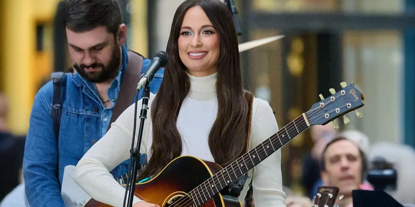 Kacey Musgraves smiles and holds a guitar on tour.