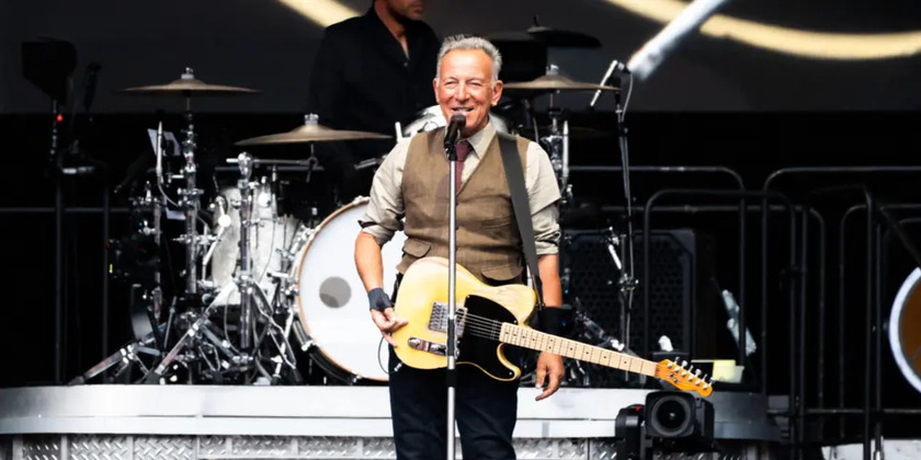 Bruce Springsteen stands on stage with a guitar.