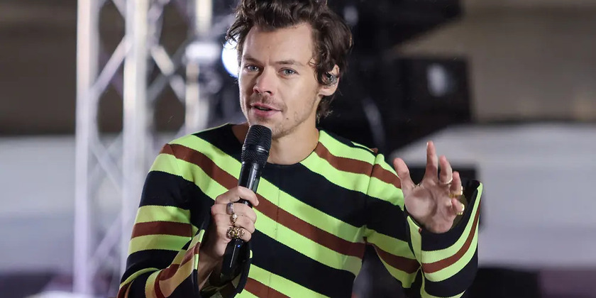 Harry Styles wears stripes and speaks into a microphone on stage.