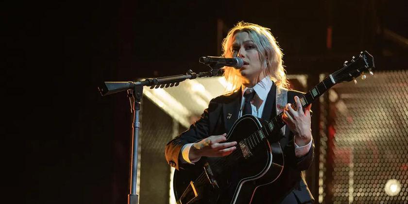 Phoebe Bridgers performs in a suit and sings with a guitar on stage.