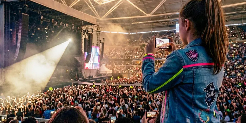 A woman films a concert on her phone in a crowd of many concert goers and phones.