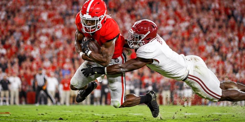 Georgia Bulldogs football player tackled by Alabama Crimson Tide defender.