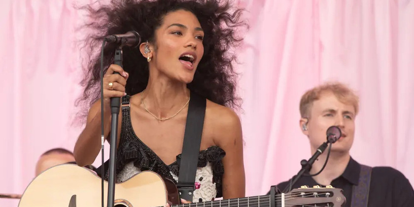 Olivia Dean performs on stage with wind-blown hair.