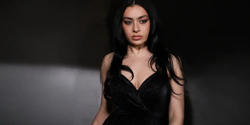 Charli xcx in a black dress on stage with a black background.
