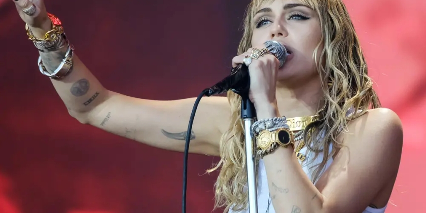 Miley Cyrus performs on stage while pointing to the sky.