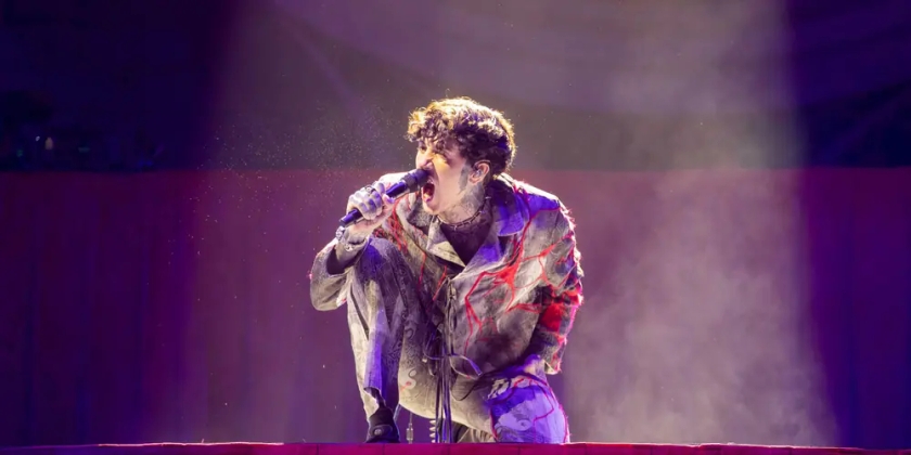 Oli Sykes, lead singer of Bring Me the Horizon, crouches on stage and sings into a microphone.
