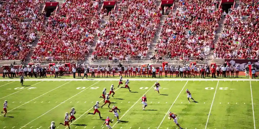 A football team in red jerseys plays in front of a large crowd. 