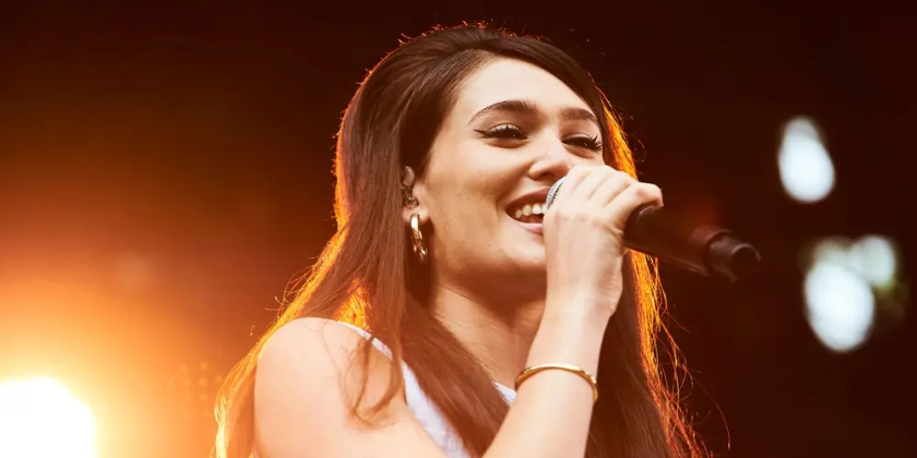Sienna Spiro performs in orange light while smiling into a microphone.