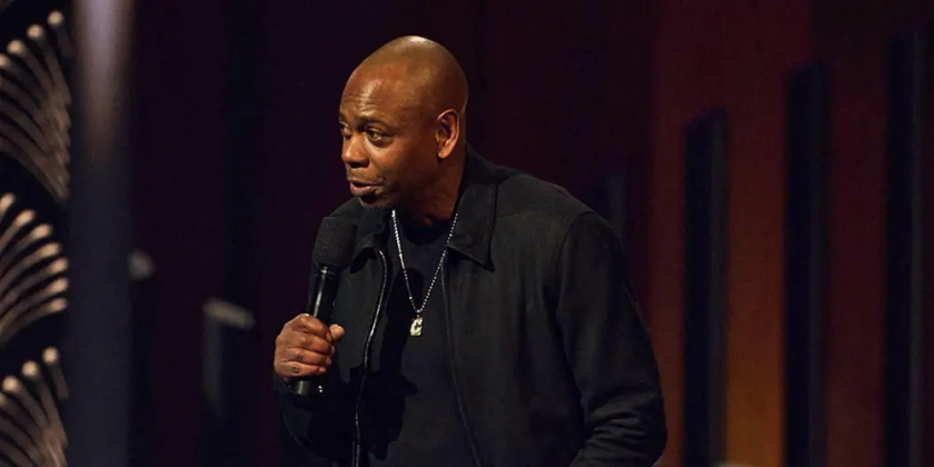 Dave Chappelle performs on stage with a microphone.