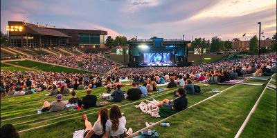 A view of Fiddler's Green Amphitheatre with a crowd on the grassy lawn watching a concert.