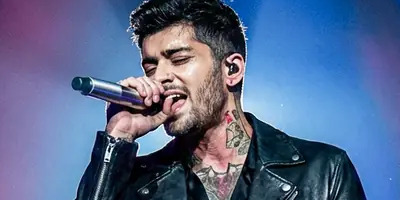 ZAYN holds a microphone to his mouth in purple lighting.