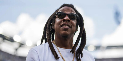 Jay-Z smiles and looks upwards, surrounded by a stadium setting.