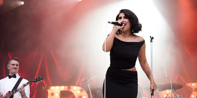 RAYE sings in an elegant dress backlit on a stage.
