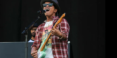 Bruno Mars sings and plays guitar on stage.