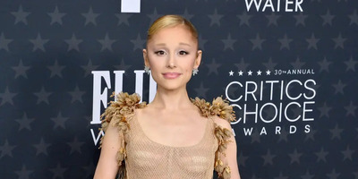 Ariana Grande stands at an awards show with her hair back looking at the camera.