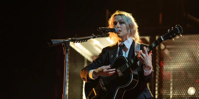 Phoebe Bridgers performs in a suit and sings with a guitar on stage.