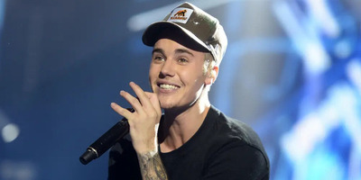 Justin Bieber smiles with a hat on while holding a microphone.