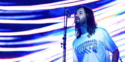 Kevin Parker sings on stage with a colorful background.