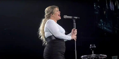Kelly Clarkson stands on stage and sings into a microphone in a black and white dress.