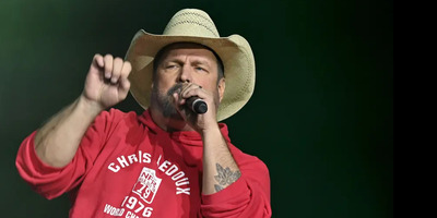 Garth Brooks sings into a microphone in a red sweatshirt.