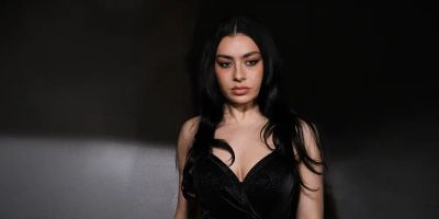 Charli xcx in a black dress on stage with a black background.