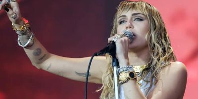 Miley Cyrus performs on stage while pointing to the sky.