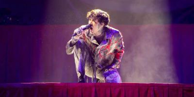 Oli Sykes, lead singer of Bring Me the Horizon, crouches on stage and sings into a microphone.