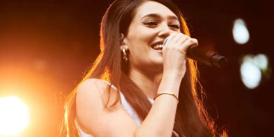 Sienna Spiro performs in orange light while smiling into a microphone.