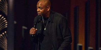 Dave Chappelle performs on stage with a microphone.